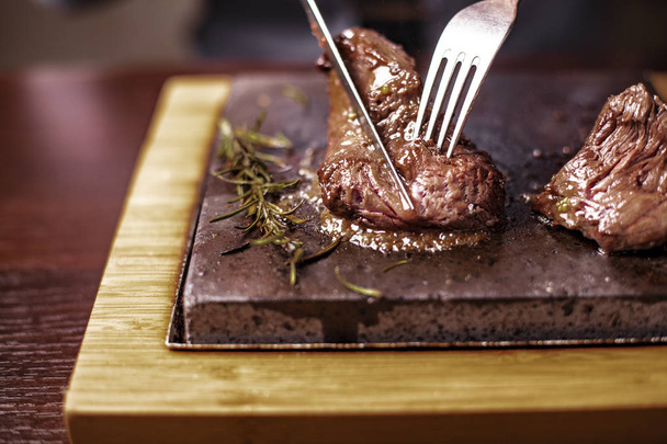 çok sıcak bir taş bıçak ve çatal ile kendi tat ahşap bir masa üzerinde bir adam tarafından pişmiş sığır filetosu biftek - Fotoğraf, Görsel