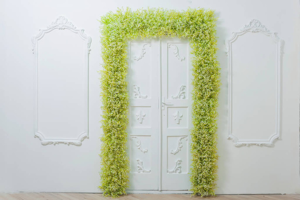 春の装飾。白い壁壁に美しい漆喰。緑と白の花のアーチ。写真ゾーン。花と戸口の装飾。白い赤ちゃんの息. - 写真・画像