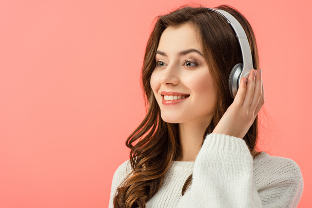 smiling and beautiful woman in white sweater listening music with headphones isolated on pink - Fotografie, Obrázek