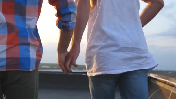 Widok z tyłu mężczyzna para trzymając się za ręce siebie i jogging na tarasie na dachu. Młodzi chłopcy gej uruchomiona do krawędzi dachu i podnoszenie broni. Piękny gród w tle. Zwolnionym tempie - Materiał filmowy, wideo