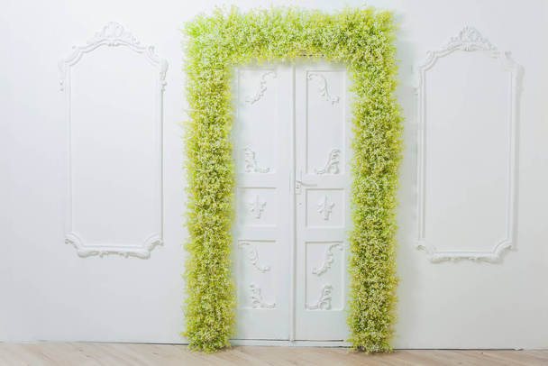 Bahar dekoru. Beyaz duvarlar. Duvarların üzerinde güzel bir alçı var. Yeşil ve beyaz çiçekler kemeri. Fotoğraf bölgesi. Çiçek ile kapı dekor. Beyaz bebeğin nefesi. - Fotoğraf, Görsel