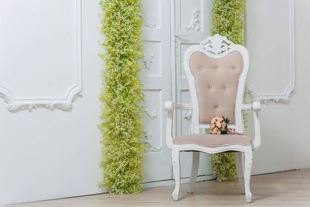 Tavaszi dekoráció. Fehér falak. Gyönyörű stukkók a falakon. Arch zöld és fehér virágok. A dekor az ajtóban a virágok. Fehér baba lehelete. A szék halvány rózsaszínű. Esküvői csokor. - Fotó, kép