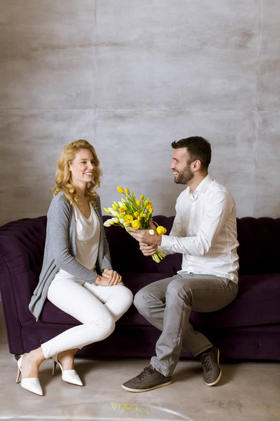 Young woman receiving a gift of  yellow tulips from her husband or partner smiling at him - Foto, Imagen