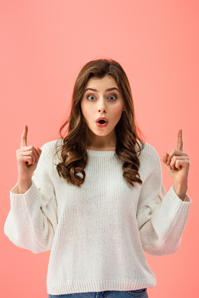 surprised and beautiful woman in white sweater pointing with fingers isolated on pink - Photo, Image