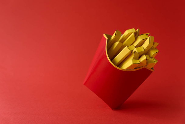 Paper French fries in red carton box on red background. Copy space. Creative or art food concept - Fotó, kép
