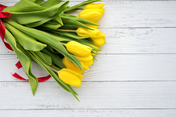 Ramo de flores de tulipanes amarillos sobre fondo de madera blanca. Esperando la primavera. Feliz tarjeta de Pascua, día de la madre, 8 de marzo. Posición plana, vista superior
. - Foto, Imagen