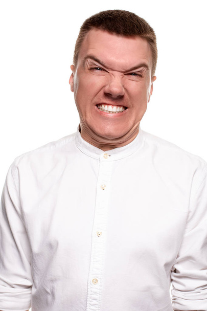 Charming handsome young man in a white shirt is making faces, while standing isolated on a white background - Photo, Image