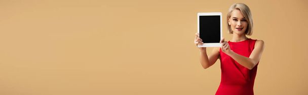panoramische opname van vrouw in rode jurk bedrijf digitale tablet met leeg scherm geïsoleerd op beige - Foto, afbeelding
