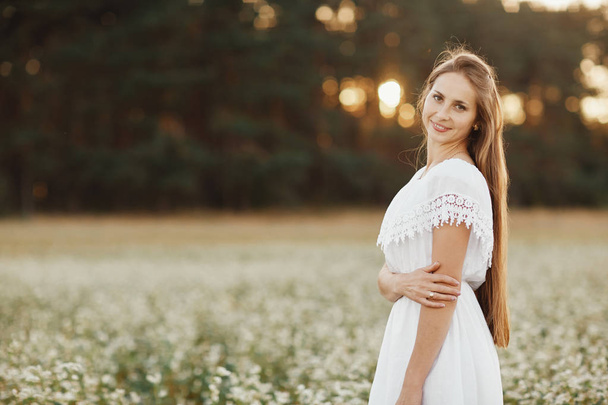 Retrato de uma menina bonita em um vestido branco em um campo de floração. Campo de flores. Verão. unidade com a natureza
. - Foto, Imagem