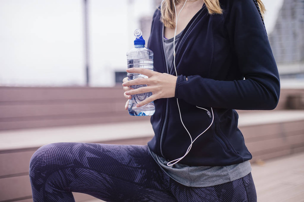 Nuori nainen on virkistävä harjoittelun jälkeen ja juo vettä ulkona
 - Valokuva, kuva