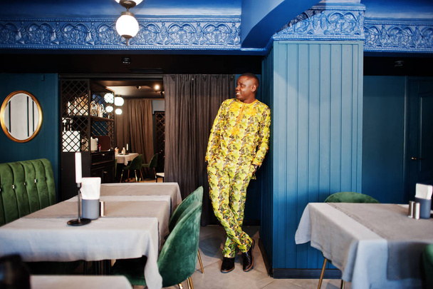 Friendly afro man in traditional yellow clothes at restaurant. - Foto, immagini