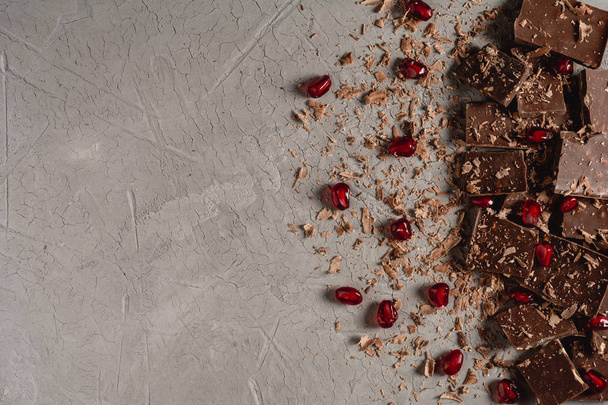 Broken chocolate pieces and chocolate powder, chocolate with hazelnut, chocolate and red pomegranate on beton background with copy paste place - Photo, Image