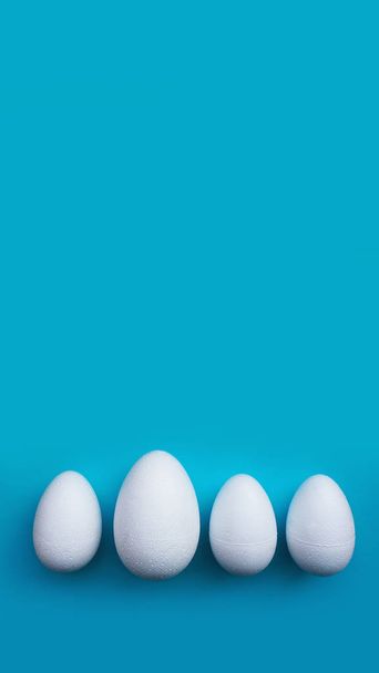 White foam eggs on blue background. Flat lay, top view. Easter concept - 写真・画像