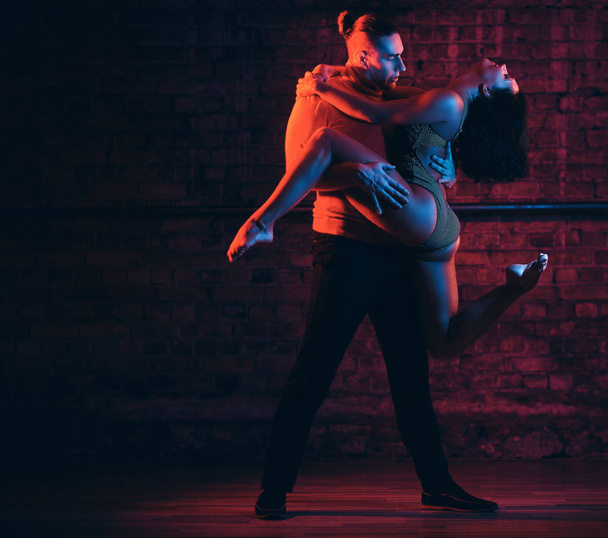 Hermosa pareja bailando en la pista de baile en un club nocturno. Bailarines actuando en la oscuridad con iluminación
 - Foto, imagen