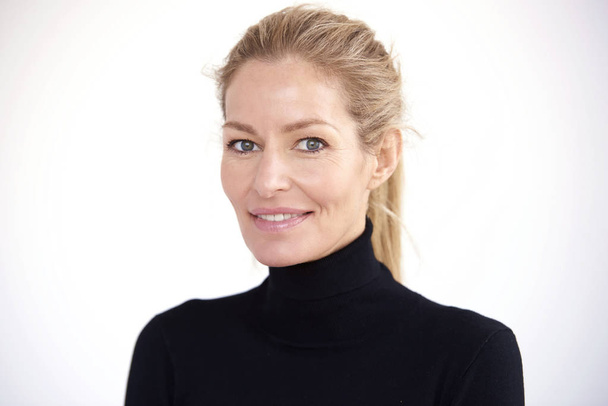 Close-up portrait of beautiful smiling middle aged woman wearing roll neck sweater and looking at camera while standing against at isolated white background.  - Valokuva, kuva