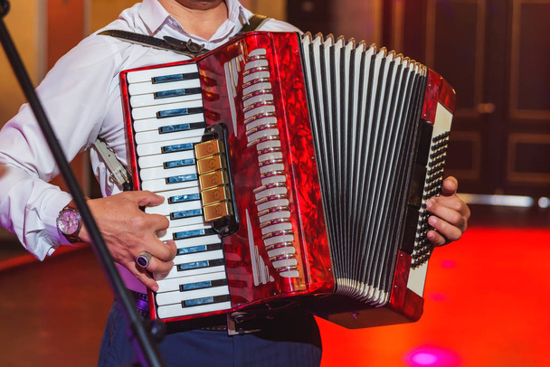 Musical instrument. A man plays the accordion. Event. Accordion. Bellows. Bayan. Keyboard accompaniment. Musical performance. Ensemble. - Photo, Image