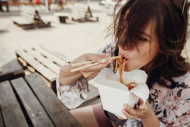 Stylish hipster girl eating wok noodles with vegetables from car - Photo, Image