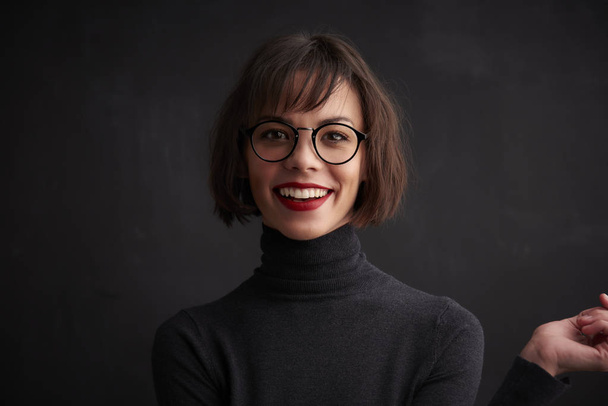 Close-up portrait shot of beautiful young woman wearing roll neck sweater and eyewear while standing at dark background.  - Zdjęcie, obraz