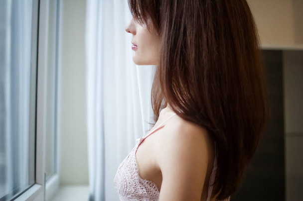 Incrível jovem mulher olhando através da janela com ternura no início da manhã em casa
 - Foto, Imagem