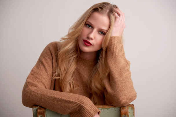 Portrait shot of beautiful young woman with blond long hair and red lipstick sitting at isolated background. - Fotó, kép