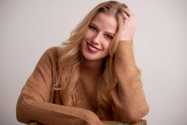 Portrait shot of beautiful young woman with blond long hair and red lipstick sitting at isolated background. - Φωτογραφία, εικόνα