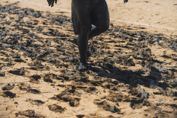 The man smeared black clay on his feet. Black clay on the body. Nature. Black healing clay. A man running on a clay surface. Wet clay in nature. Reservoir. - Photo, Image