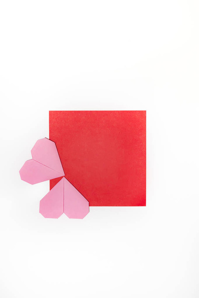 Coeurs origami artisanal rose décorer un morceau de papier rouge sur un fond blanc avec espace de copie. Carte de Saint-Valentin. Vue du dessus
 - Photo, image
