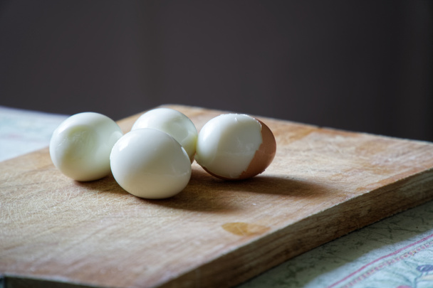 Hard boiled eggs with shell beside on wooden board - Foto, afbeelding