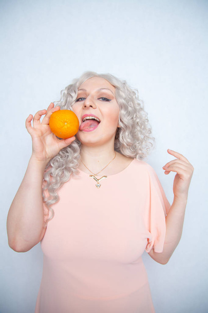 charming plump curly blonde in pink dress with orange on white solid studio background alone - Photo, Image