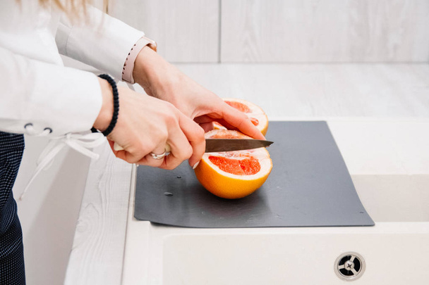 Kadının kesme taze greyfurt mutfak üzerinde eller. Kız kesme bıçağı portakallı. Sağlıklı yaşam konsepti. - Fotoğraf, Görsel