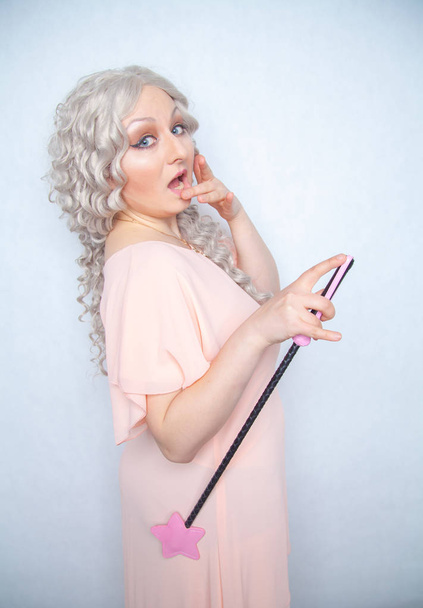 ピンクの星乗馬鞭と変態きれいな女性。かわいい金髪の女性は、白色固体のスタジオの背景に bdsm 鞭を保持しています。. - 写真・画像
