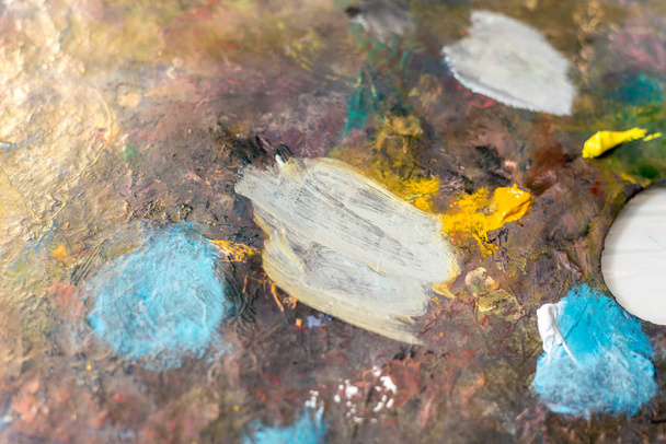 Paints of different colors on a multi-colored palette of mixed oil paints - Photo, Image