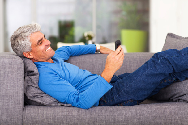 keski-ikäinen mies lukemassa tekstiviestiä matkapuhelimella
 - Valokuva, kuva