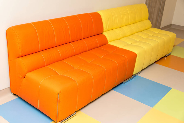Два разноцветных желтых и оранжевых дивана на цветном полу
 - Фото, изображение