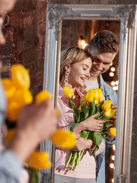 Beaming beautiful woman holding yellow tulips standing near husband - Fotografie, Obrázek
