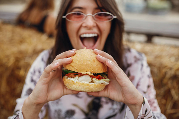 Φαγητό του δρόμου φεστιβάλ. Κομψό hipster κορίτσι σε γυαλιά ηλίου που τρώει  - Φωτογραφία, εικόνα