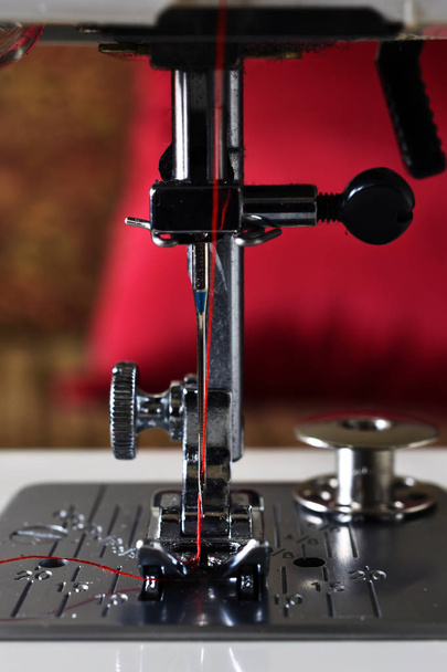 Een close-up beeld van een naaimachine naald met heldere rode draad.  - Foto, afbeelding