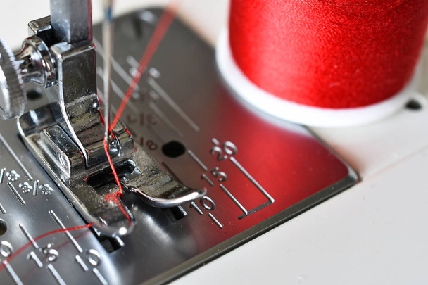 Una imagen de cerca de una aguja de máquina de coser con hilo rojo brillante
.  - Foto, imagen