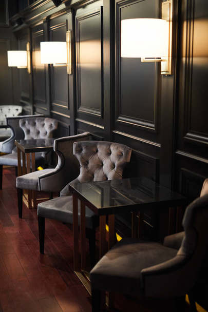Plusieurs tables et fauteuils debout le long des murs en bois noir avec des lampes à l'intérieur restaurant chic
 - Photo, image