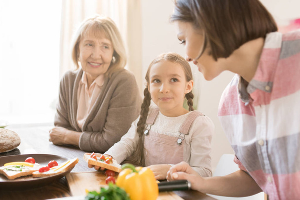 Carino bambina facendo panini con pomodori e ascoltando i suoi consigli mamma sulla cucina
 - Foto, immagini