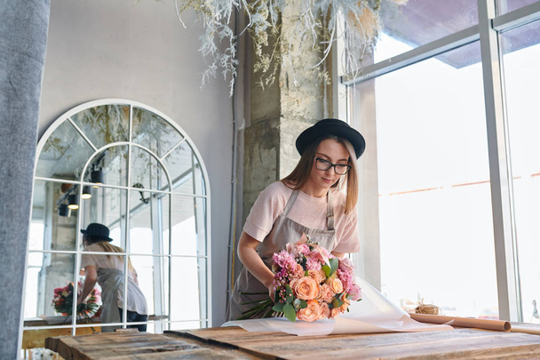 Fiorista professionista in abbigliamento da lavoro mettendo mazzo di fiori freschi pastello su un pezzo di carta da imballo in studio
 - Foto, immagini