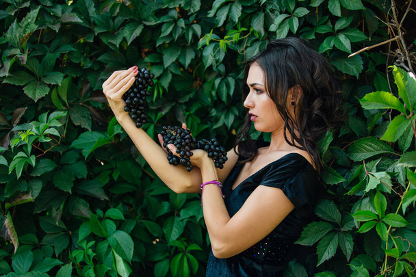 Portrait of young sexy brunette biting black grapes. - Photo, image