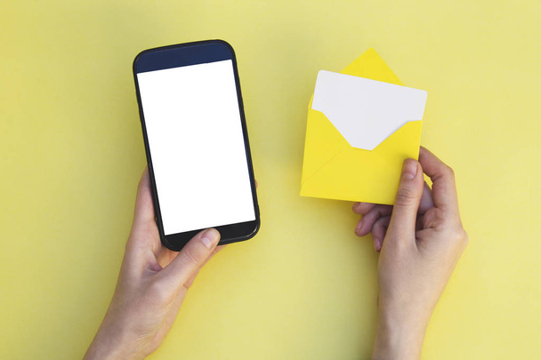 Woman hands holding mobile phone and envelope on yellow background. - Photo, Image