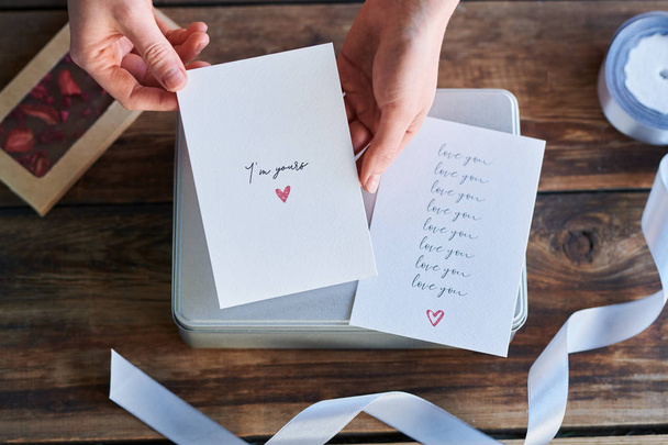Вид зверху рук людини, що тримає вітальну листівку ручної роботи на день Святого Валентина над подарунковою коробкою
 - Фото, зображення