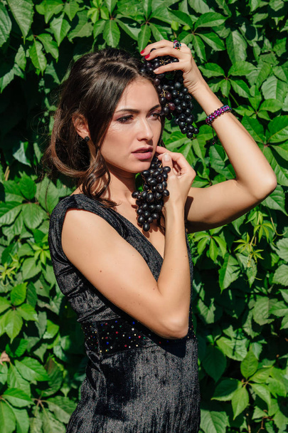 Portrait of young sexy brunette biting black grapes. - Fotografie, Obrázek