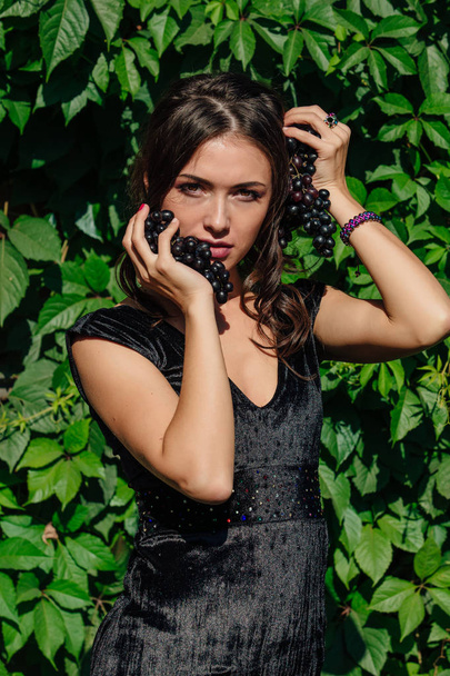 Portrait of young sexy brunette biting black grapes. - Φωτογραφία, εικόνα