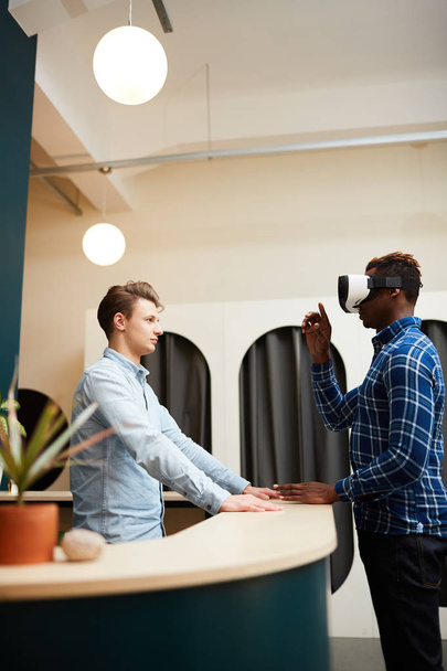 Afro-Américain avec casque de réalité virtuelle parlant à son collègue au comptoir devant
 - Photo, image