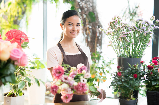 Happy brunette tyttö työvaatteet katselee sinua seistessään työpaikalla joukko tuoreita kukkia kukkakauppa
 - Valokuva, kuva