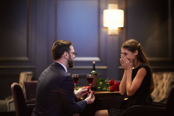 Zaskoczony dziewczyna ukrywa jej twarz w dłonie podczas młody mężczyzna Dokonywanie wniosek jej w restauracji na Walentynki - Zdjęcie, obraz