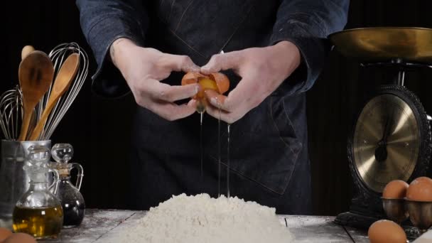 Detailní záběr mužské šéfkuchař praskání vejce v míse s moukou. Zpomaleně padající vejce do mouky v UK. Jídlo záběry. Vejce do mouky, zpomalené. Žloutek Falls. Potraviny Blog, moučné výrobky - Záběry, video